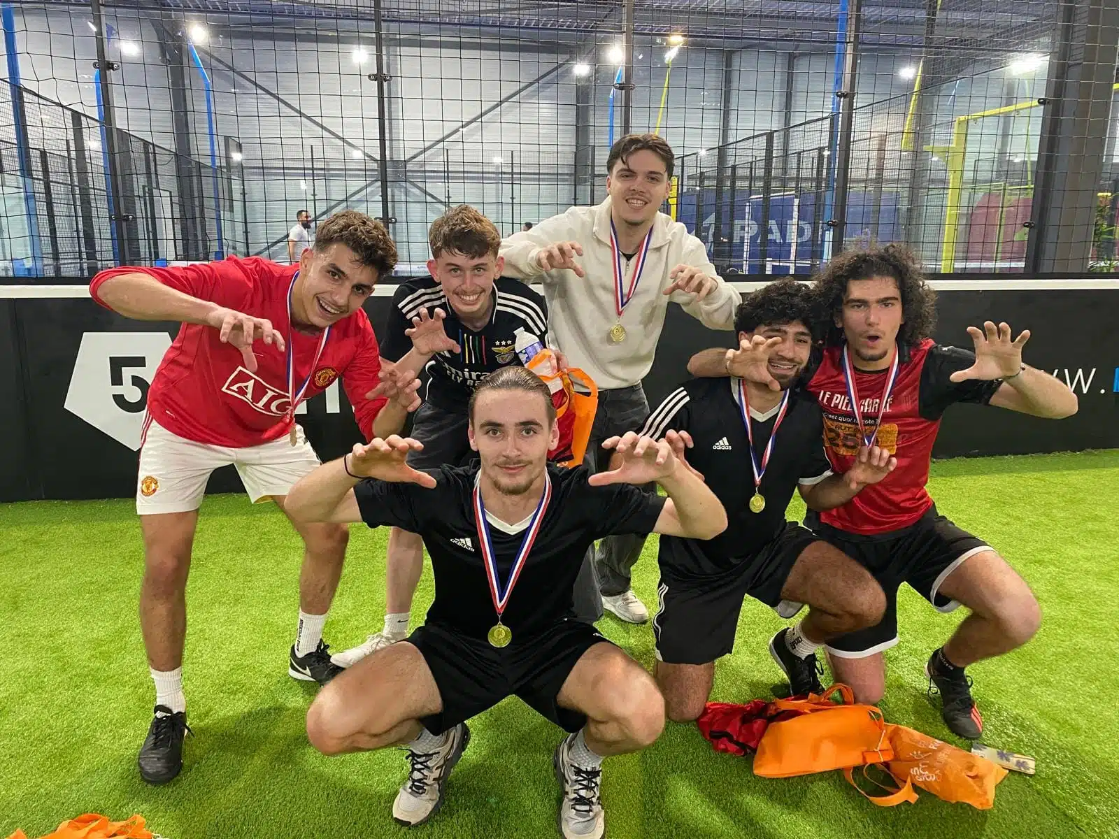 Équipe de jeunes sportifs célébrant leur victoire dans un terrain de football indoor, portant des médailles et adoptant une pose énergique.