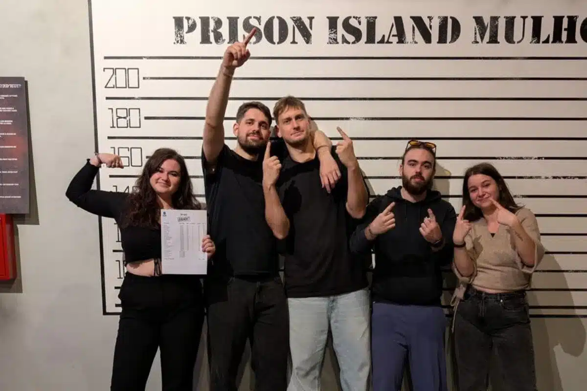 Un groupe d’étudiants sourit devant la caméra après avoir participé à l’activité Prison Island. Ils posent ensemble dans un décor rappelant l’univers du jeu, certains tenant des cartons de points ou des accessoires fournis par l’établissement.